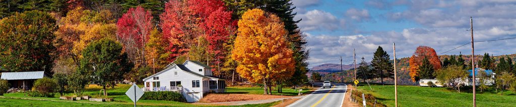 A country road winding by a white barn with bright autumn colored trees