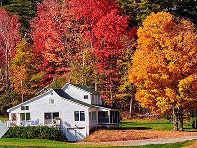 A New England farmhouse in front of colorful autumn trees